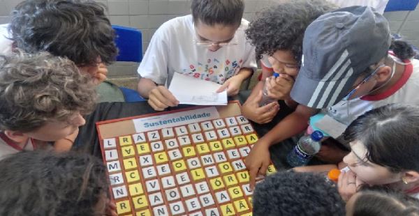 Foto com 7 estudantes jogando um caça-palavras com o tema sustentabilidade. Jogo tamanho ampliado. 
