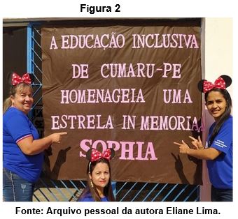 A imagem evidencia três professoras da Sala de Recursos Multifuncional que estão usando blusas e calças azuis, e tiaras da Minnie, duas estão em pé ao lado de uma faixa e apostando com os indicadores para a faixa que diz (A EDUCAÇÃO INCLUSIVA DE CUMARU – PE HOMENAGEIA UMA ESTRELA IN MEMORIAN SOPHIA) e a terceira professora está agachada na frente desta faixa. 