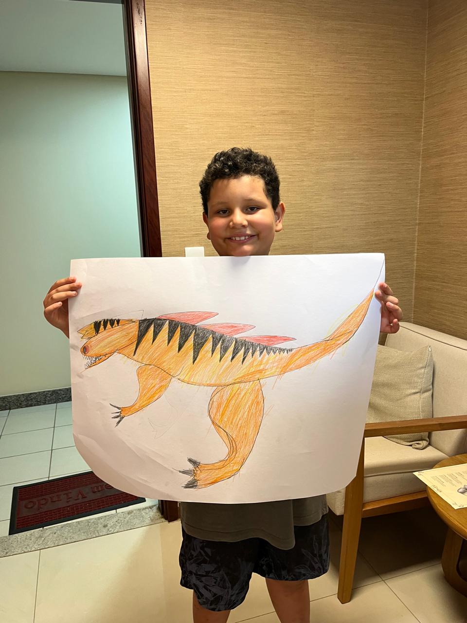 Menino sorridente segura um desenho colorido e detalhado de um dinossauro.